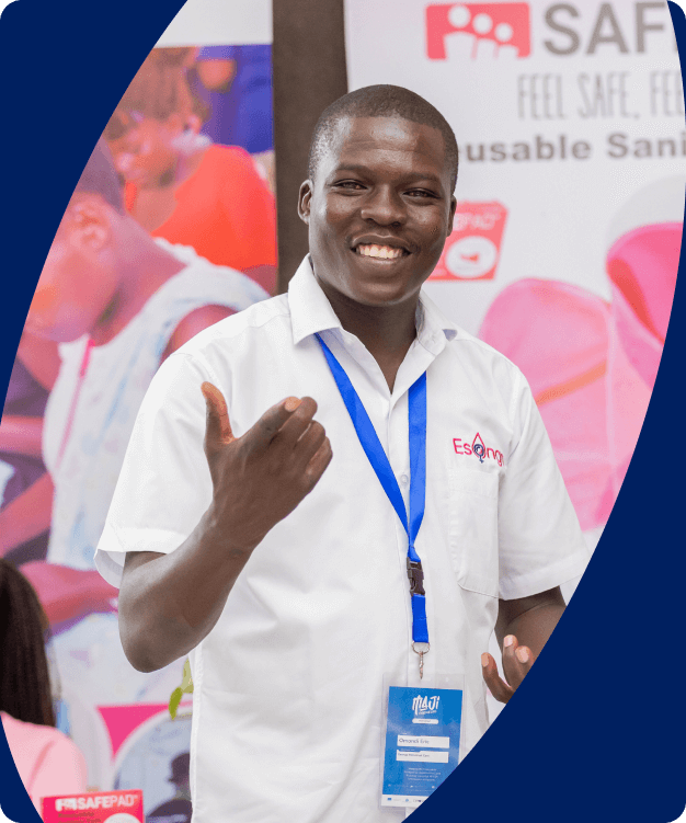 A black man with a badge around his neck smiles as he points his finger at the camera; he is at an event.